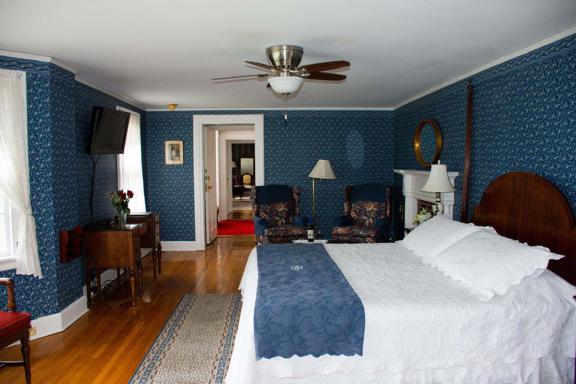 Main House Suite bedroom with wooden floor, a king-size bed, sitting area, TV, ceiling fan